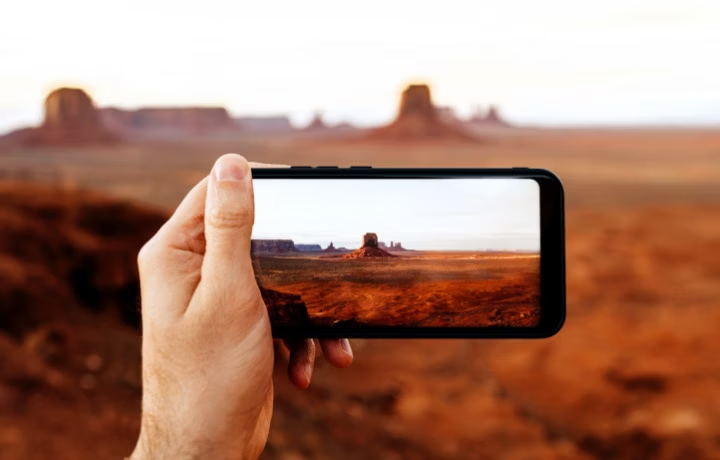 Hand holding smartphone with photograph of Monument Valley rock formations with out-of-focus desert landscape in background