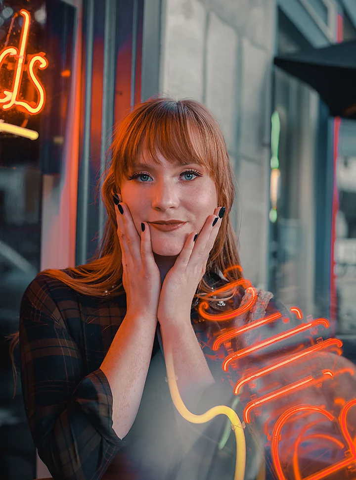 A portrait photo of a person next to a neon sign that is superimposed in the lower right of the photo