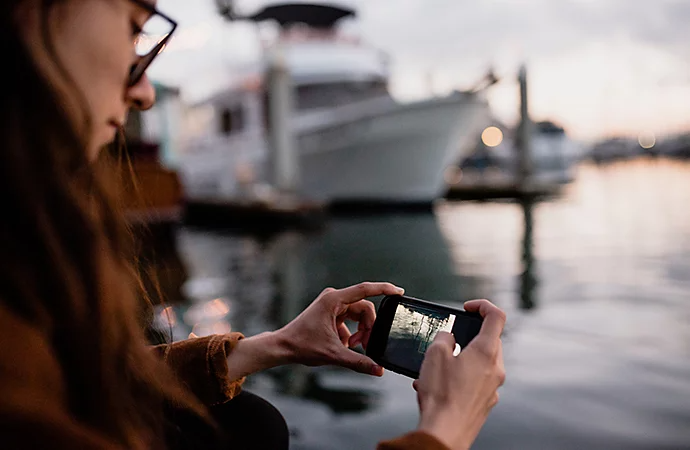 A mobile photo of a photographer looking at their DSLR camera while standing on a coastline