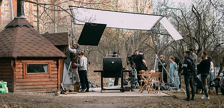 A production crew arranging a video set around a small cabin hut in a park