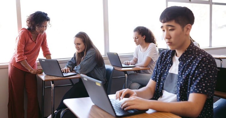 A teacher and their students using laptops to review schoolwork in a classroom