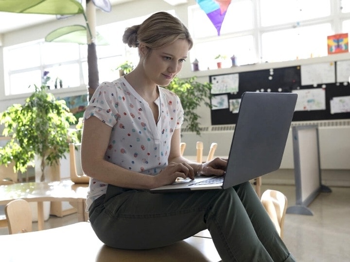 A person sitting on toddler desk using their laptop to review homework in a classroom