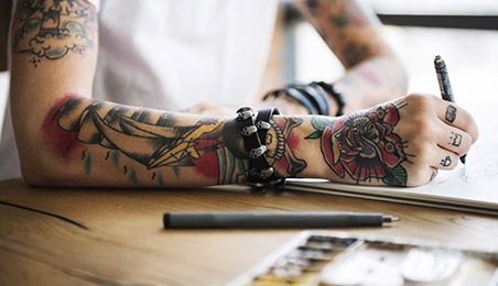 A tattoo artist draws a new tattoo design on a sketch pad