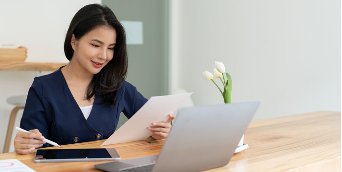 Mujer leyendo un documento mientras usa tablet y una laptop