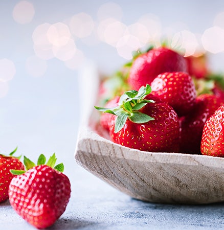 Close up picture of strawberries in a bowl with bokeh background.