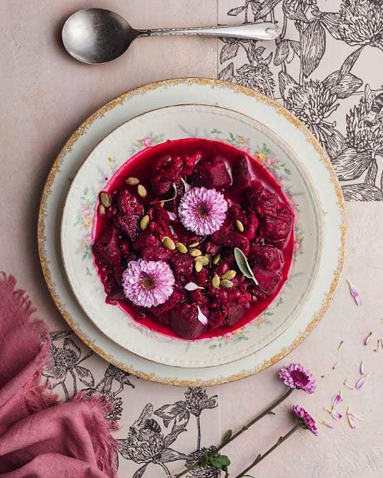 An artistic flat lay photo of flowers in a teacup filled with red liquid and surrounded by decorations