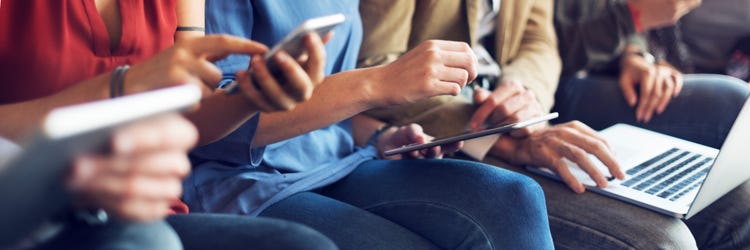 Torsos and hands of four people interacting with tablets, phones and a laptop.