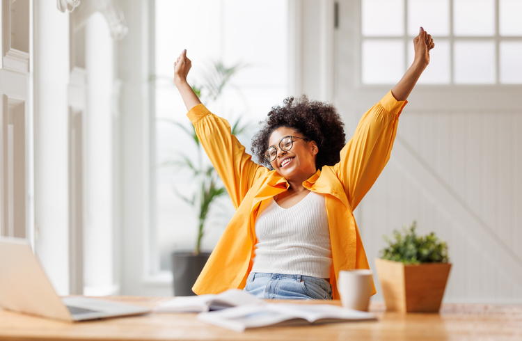 Woman sitting at a laptop and smiling holding hands up in air indicating success.