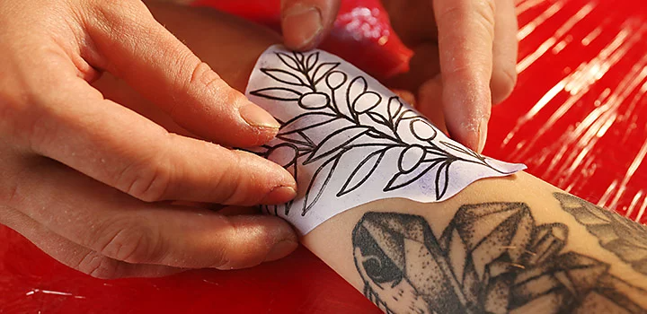 Tattoo artist gets ready to trace a new tattoo design on a client's arm