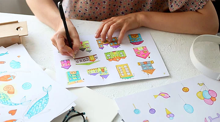 A kid making cartoon drawings of buildings and fish at a table