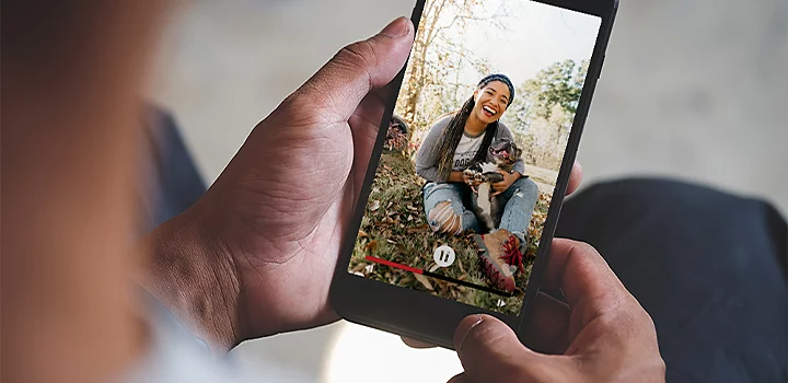 A person watching a vertical video on their mobile phone of a person sitting in grass with their dog in their lap