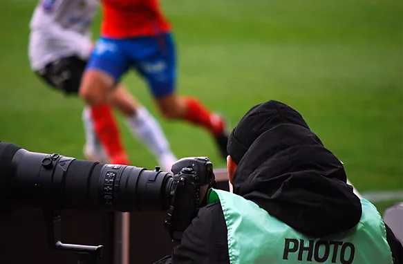 A photo of a sports photographer from behind at a soccer game.