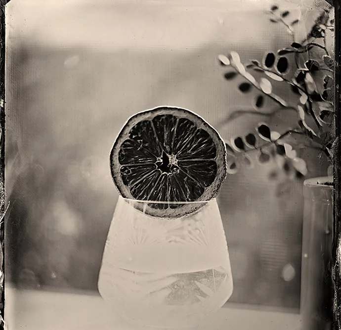 A tintype photo of an orange over a glass