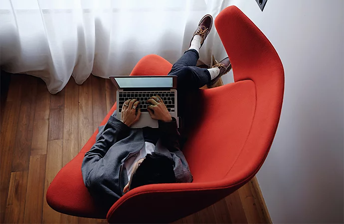 A person editing video on their laptop while lying in a large chair