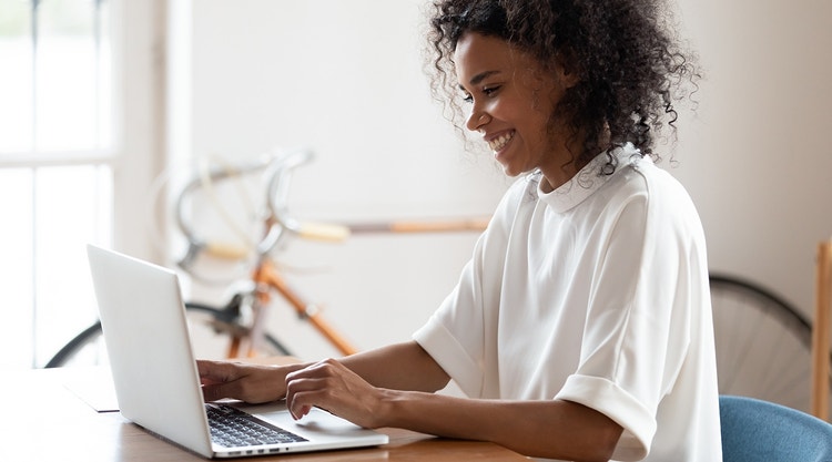 A woman in a white shirt at a desk using a laptop to sign an NDA with Adobe Sign.