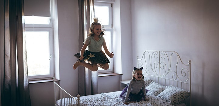 Two little girls dressed up jumping on a bed.