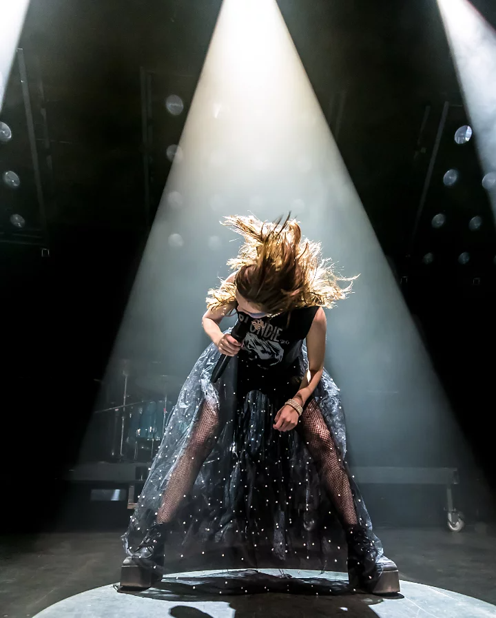 A singer hunched over, singing in a spotlight onstage