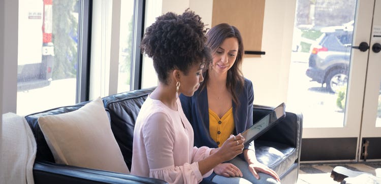 Dos personas sentadas en un sofá una junto a la otra mirando una tablet