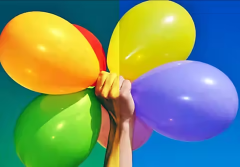 An image of a hand holding colorful balloons. The colors in half of the image are more vibrant than the other half.