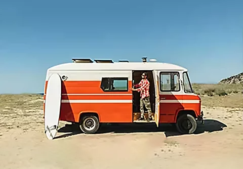 A photo of a van parked on the beach with a person prepping to go surfing.