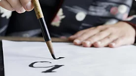 A photo of a person hand-drawing letters with a brush on paper.