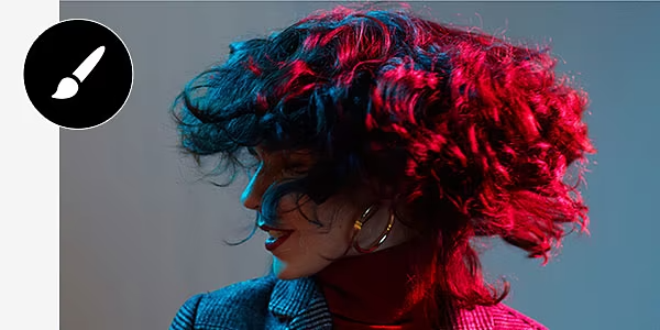 A person in a plaid jacket with voluminous shoulder-length hair is profiled in motion bathed in red light