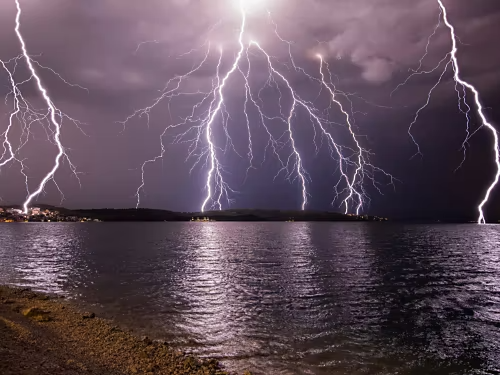 An image of a lake at night. The sky is filled with lightning.