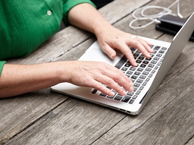 A person sitting at a picnic table and working in Adobe Acrobat on their Mac to combine several files into one PDF