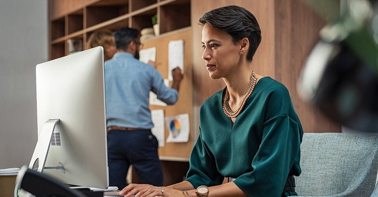 A businessperson sits at a desk working on a desktop computer