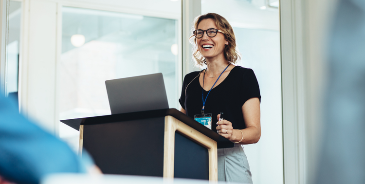 A female business professional develops the professional skill of public speaking by presenting at an event.