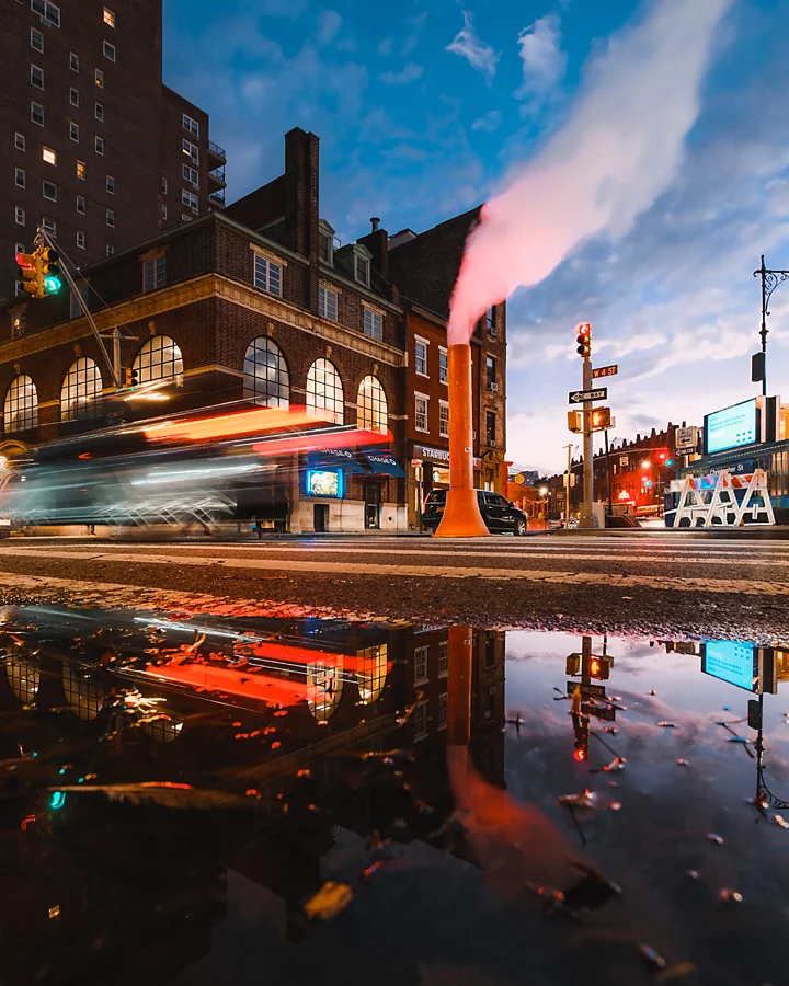 A light trail of a car driving by a building and a ground exhaust vent in a city