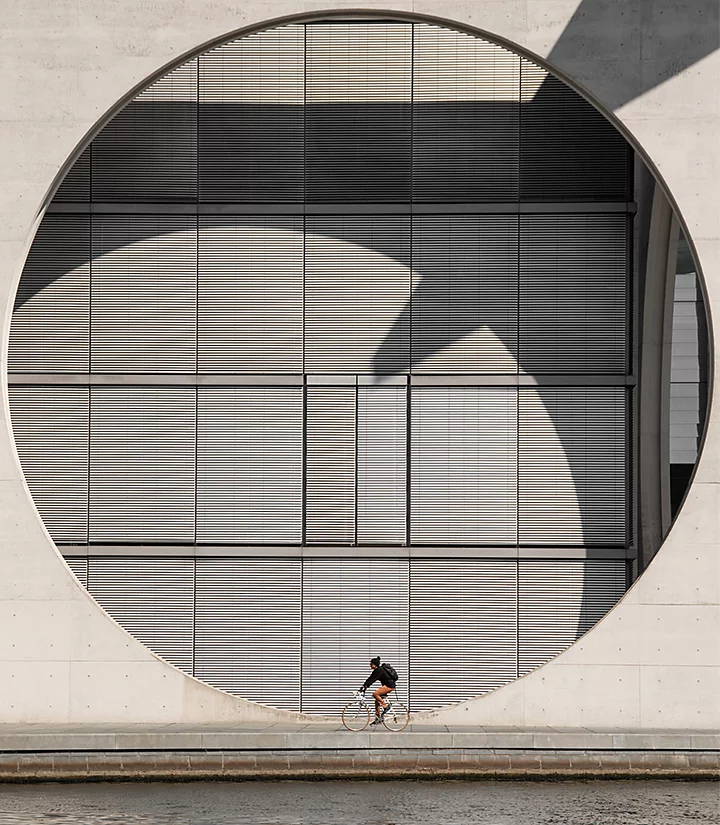 Person biking in front of a large die-cut circle in front of a building