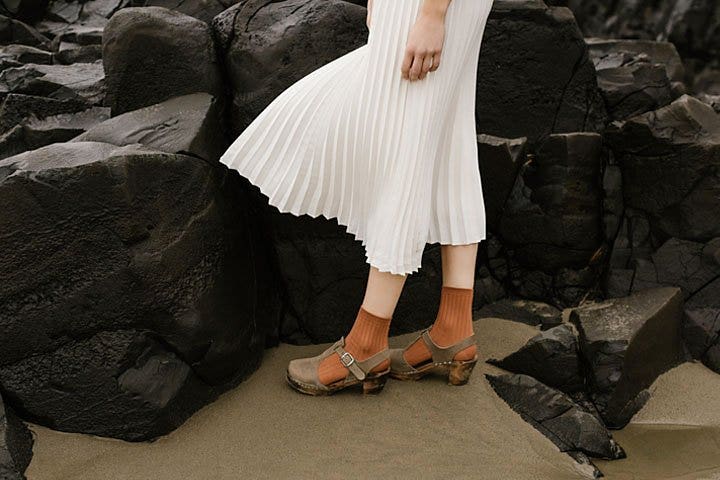 A close-up of a person's legs standing in front of rocks on a beach creating highlights and shadows