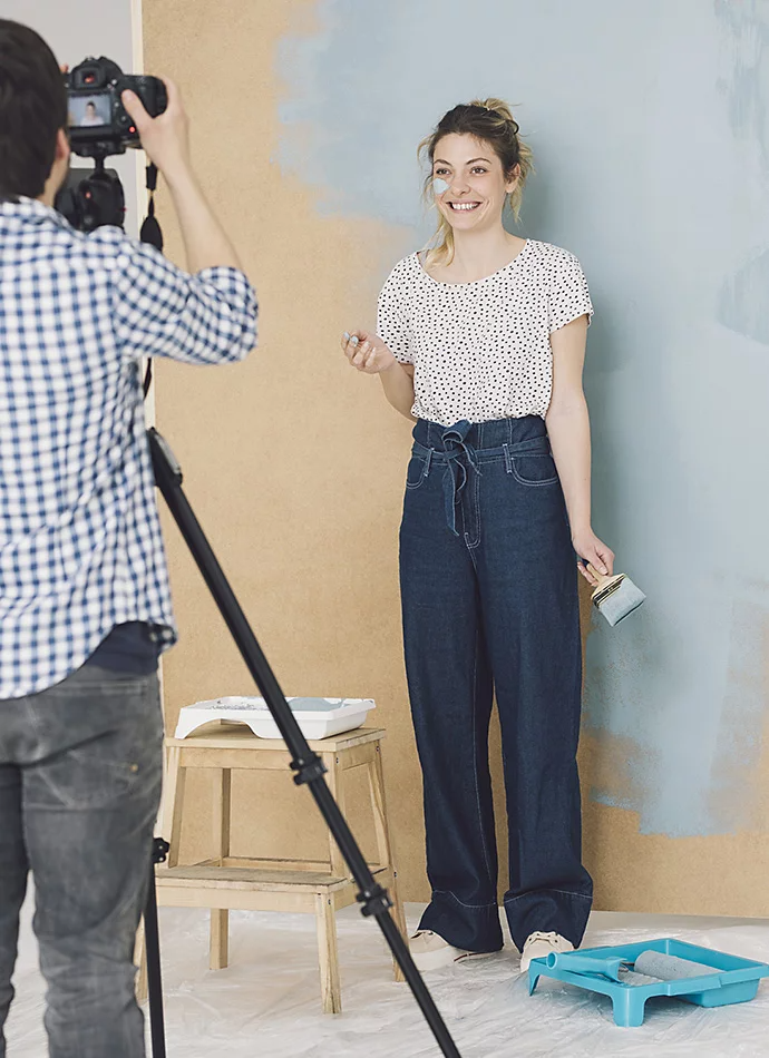 A photographer taking a photo of a model standing in front of a recently painted wall while they hold a paintbrush