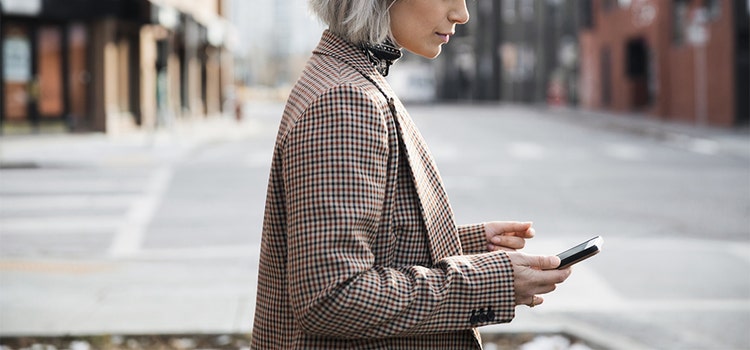 A person walking and staring down at their mobile phone with a patterned jacket which shows aliasing