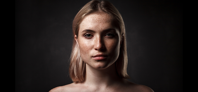 A portrait photo of a person with freckles on a black background.