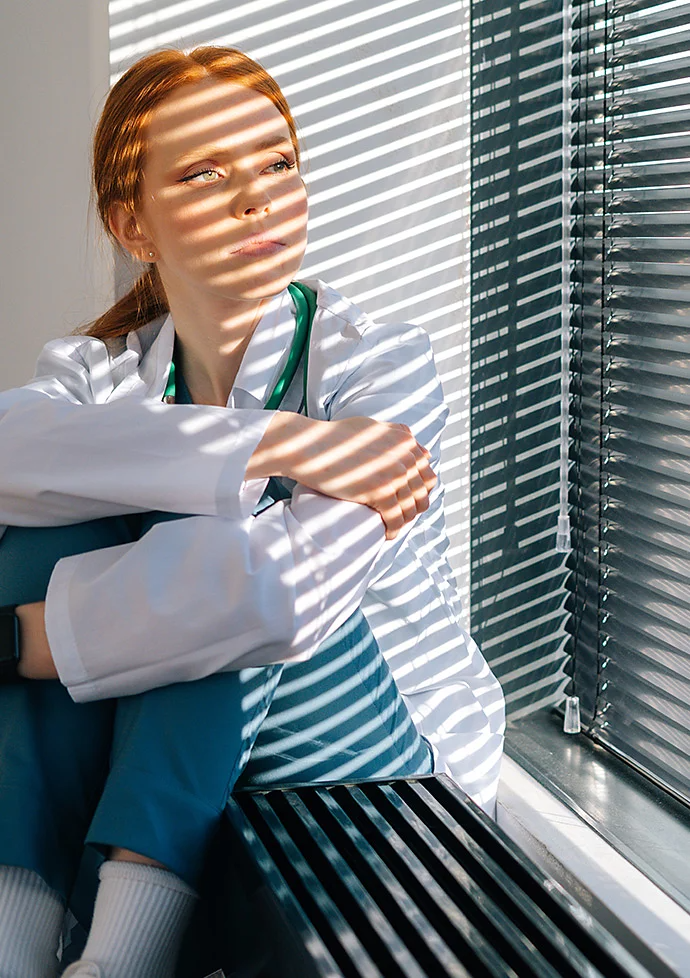 Photo of a person sitting and posing in front of a window with its blinds closed