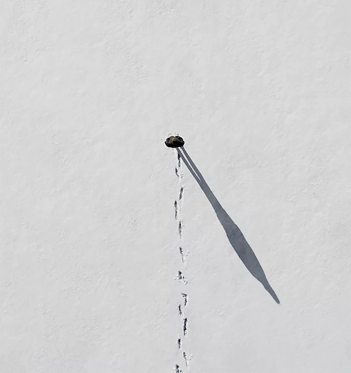 An overhead photo of a person walking in a straight line in the snow with a trail of footprints behind them