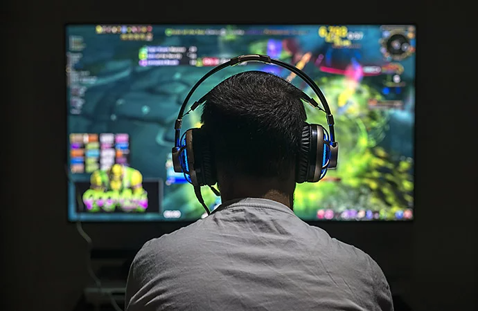 Photo of a person with headphones on, playing video games on a large screen