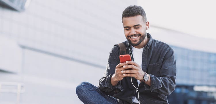 A person wearing headphones and smiling while looking at a mobile device