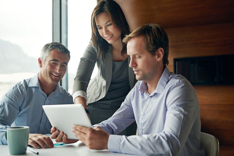 Photo of three business associates collaborating on a tablet.