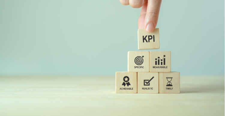 Photo of a person’s hand stacking six wooden blocks into a pyramid with KPI at the top, and blocks representing specific, measurable, achievable, realistic and timeliness underneath.