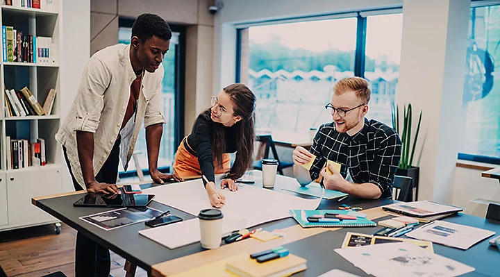 Two men and a woman at a desk having a discussion over design materials.