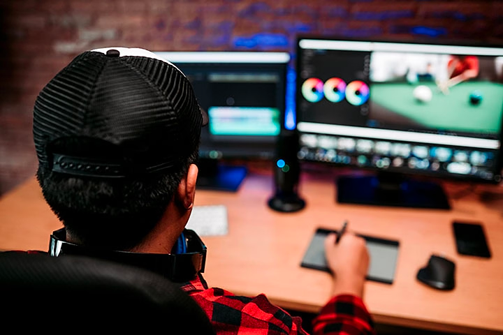 Man at desk drawing on design pad in front of two computer monitors.