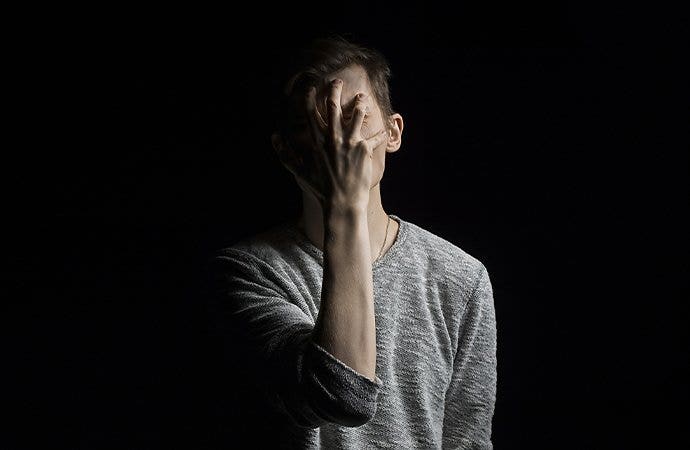 A person grabing their own face spotlighted from the side in a completely dark room