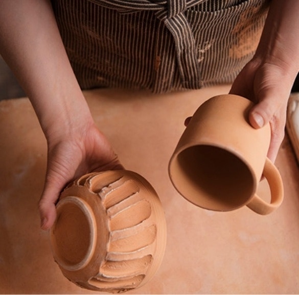 Close-up of a craftsperson showing the finer details of the unfired clay bowl and mug they are holding