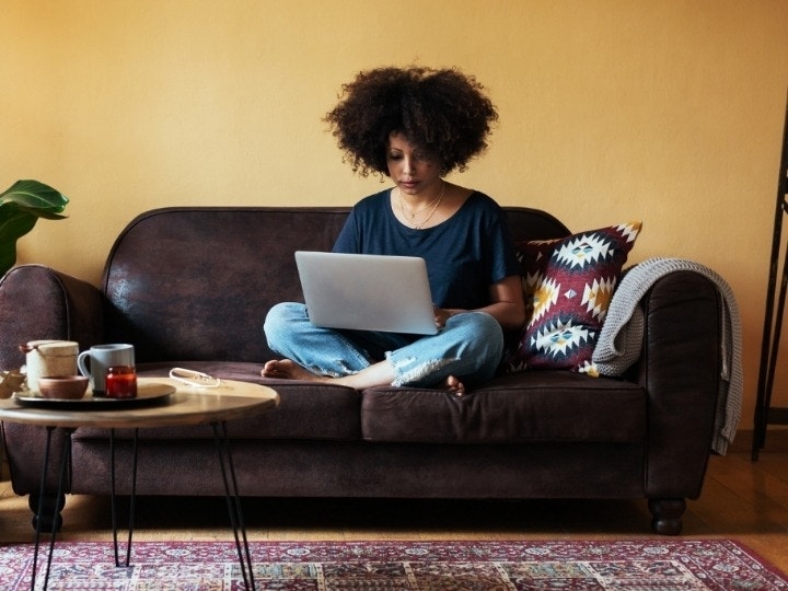 Someone sitting on their dark brown living room couch while working on a Mac editing PDFs in Adobe