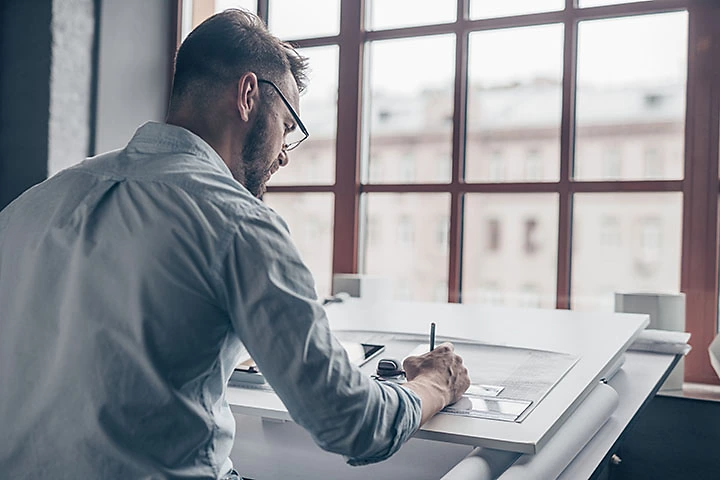 Man sat at desk sketching on a piece of paper.