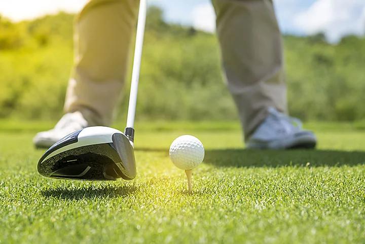 Close up of person about to hit a golf ball on the tee.