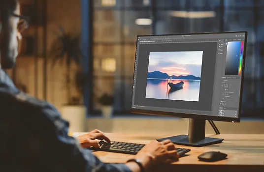 A photographer editing a photo of a log in shallow water in front of a mountain range with the sun setting behind it